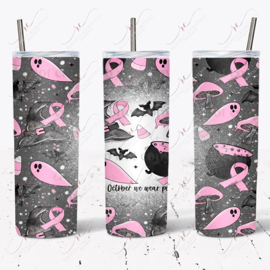 seamless halloween design. Dark grey background with white and pink dots and stars. The foreground has a black cauldron with pink potion bubbling out. Black bats and witches hats, pink candy corns, pink ghost, pink mushrooms, and a pink breast cancer awareness ribbon. The words In October we wear pink are written on 1 side of the design with a splattered bleach effect. 
