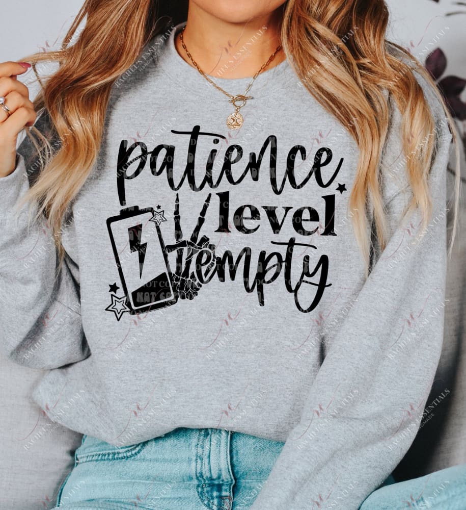 a model wearing a grey sweatshirt featuring a halloween design. The design has the words patience level empty with a low leve battery life and a skeleton hand throwing up the peace sign. 