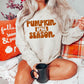blonde model wearing a tan sweatshirt with orange words saying pumpkin spice season