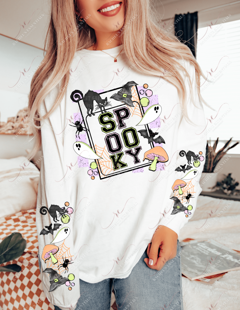 Model wearing a wearing a white long sleeve shirt with a halloween design on the front and on the sleeves. The front shows an image with the words spooky and a black cat, witches hat, ghosts, bats, spiders and mushrooms surrounding it. The sleeve features the same design without the wording. 