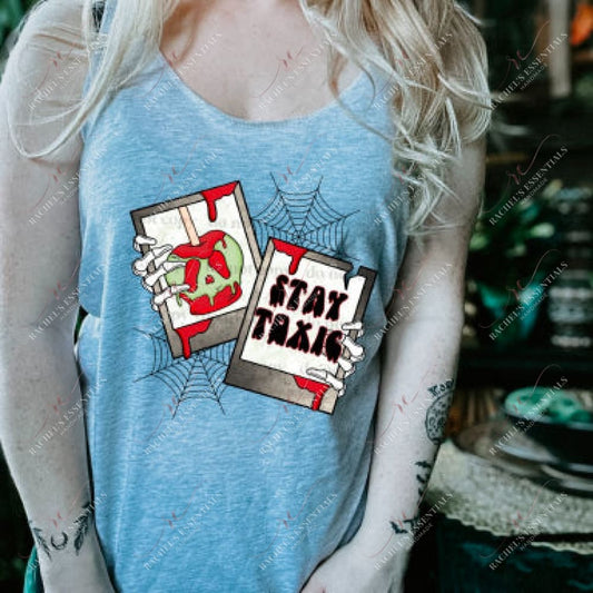 a blonde model wearing a grey tank featuring a halloween design. The design has 2 spider webs in the background with 2 polaroid pictures in front. Skeleton hands are holding the pictures. 1 picture is a candy apple with blood dripping from it and the other says stay toxic with blood dripping from the photo