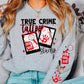 Model wearing a grey sweatshirt with a true crime tattoo studio. The design features two pictures with a red bleach bottle and magnifying glass in one and a bloody hand print and knife in the other. Blood splatter, a hand print, bleach, and magnifying glass are featured on the sleeve on the sweatshirt. 